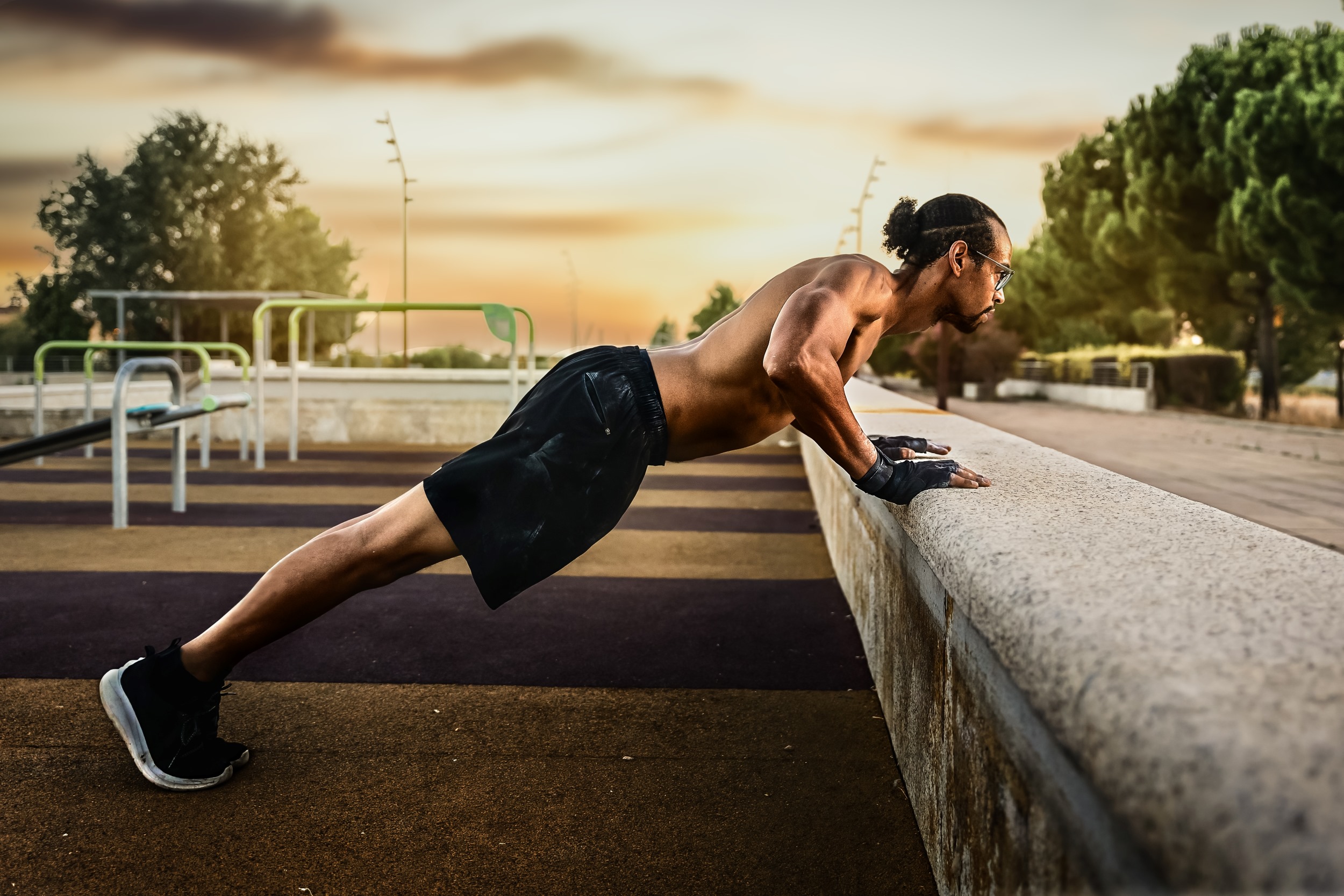 shirtless man outside sunset doing incline pushup on wall.