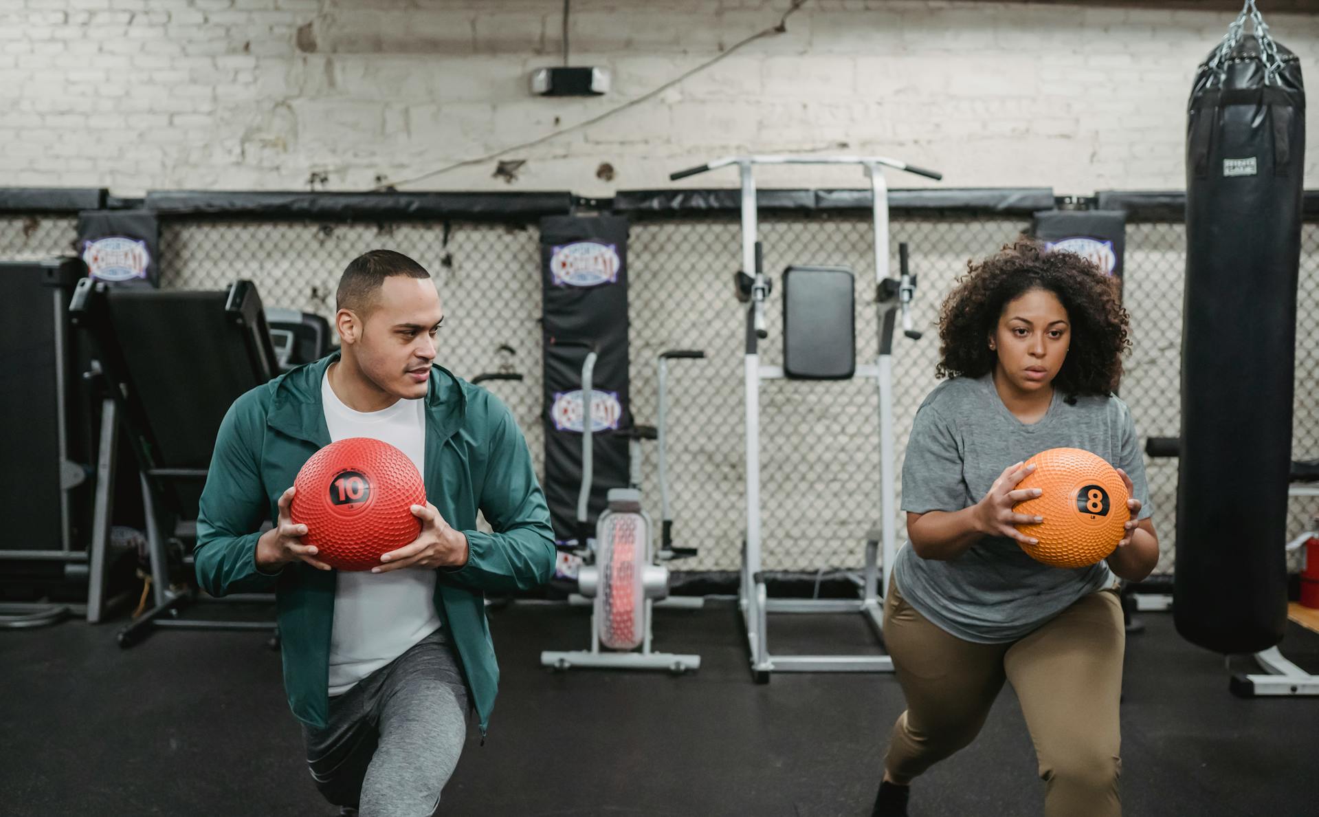 man and woman performing lunges in gym holding medicine ball