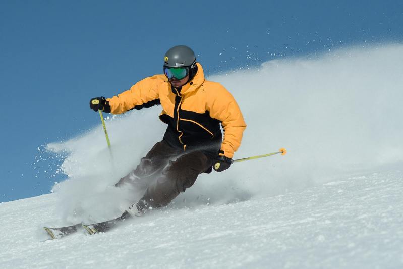 man skiing on slopes wearing yellow jacket nordic poles sunglasses